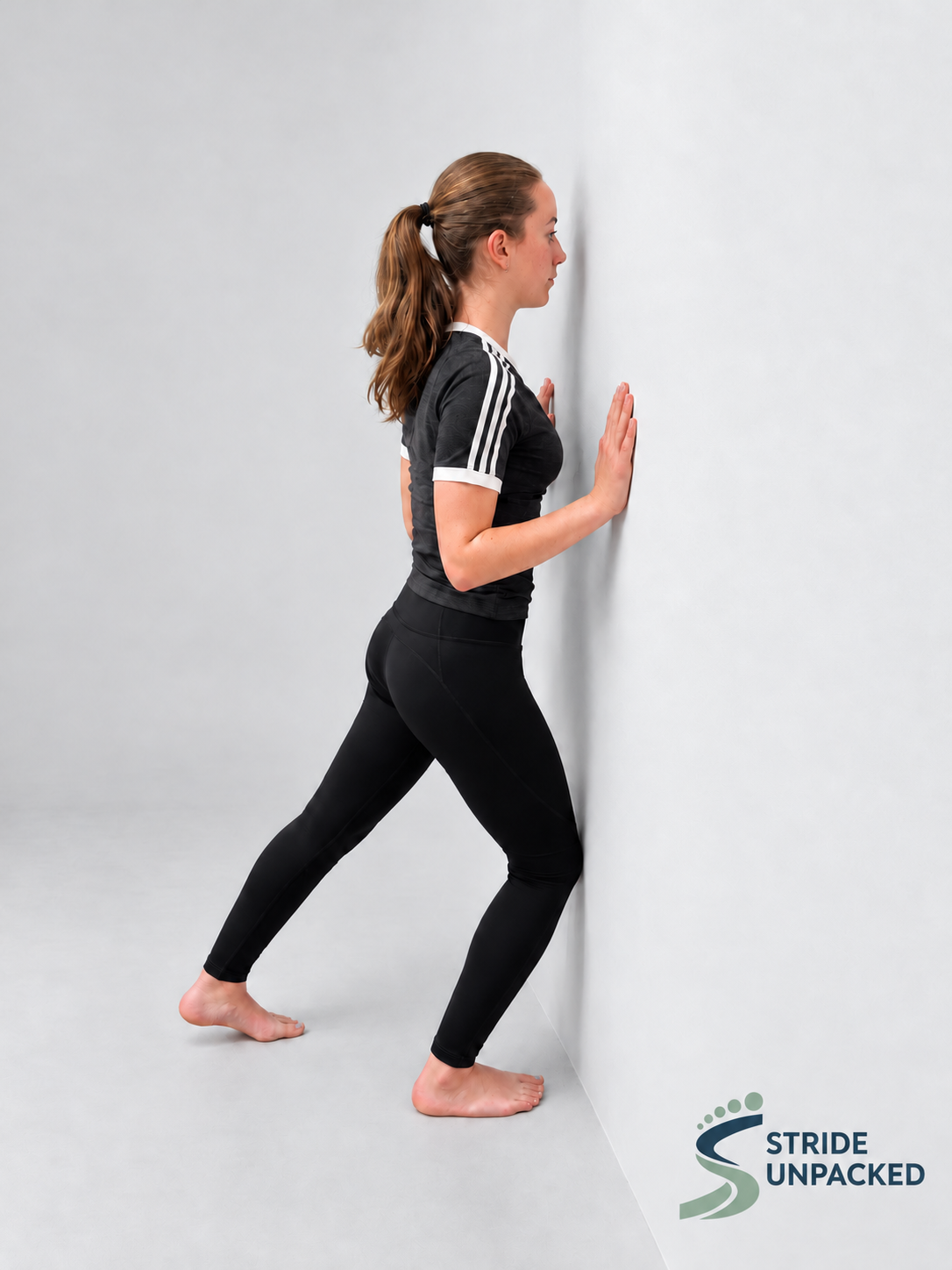 Person performing a knee-to-wall stretch with the front knee towards the wall and the front heel grounded.